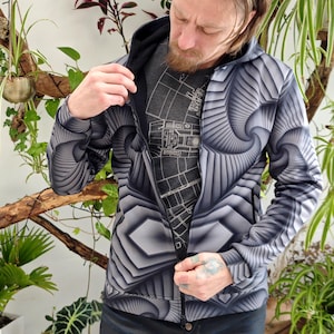 May include: A black and white hooded jacket with a geometric pattern. The zipper is partially open, revealing a gray t-shirt underneath.