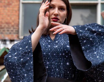 May include: A dark blue kimono featuring a white geometric constellation pattern of interconnected lines and dots. The garment has wide, loose sleeves and a solid black fabric waistband. The fabric has a smooth texture and a deep navy base color.
