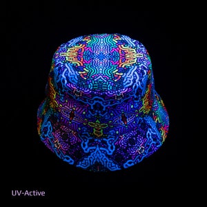 Puede incluir: Un gorro de pescador negro con un patrón psicodélico colorido que brilla bajo la luz UV. El patrón presenta remolinos, puntos y líneas en tonos de azul, verde, rosa y amarillo. El gorro está etiquetado como "UV-Active".