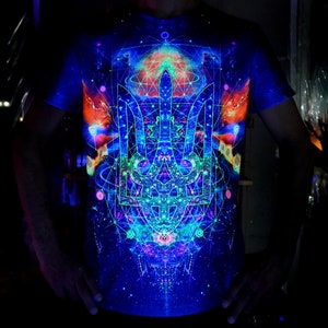 Könnte beinhalten: Ein kurzärmeliges T-Shirt mit einem leuchtenden, lebendigen Design. Das Shirt zeigt ein komplexes geometrisches Muster in Blau-, Grün-, Orange- und Lilatönen. Das Design umfasst ein zentrales Emblem und komplizierte Linien, die einen psychedelischen Effekt erzeugen. Das Shirt wird mit Schwarzlicht beleuchtet.