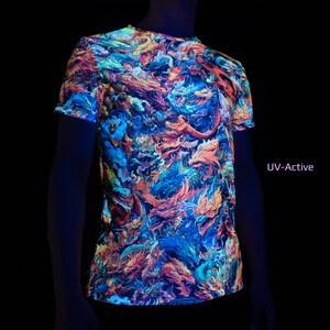 May include: A short-sleeved t-shirt with a vibrant, all-over dragon design in shades of orange, blue, and purple. The shirt is labeled "UV-Active" and glows under UV light. The design features detailed illustrations of mythical creatures.