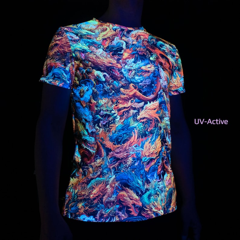 May include: A short-sleeved t-shirt with a vibrant, all-over dragon design in shades of orange, blue, and purple. The shirt is labeled "UV-Active" and glows under UV light. The design features detailed illustrations of mythical creatures.