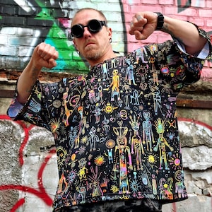 Puede incluir: Camiseta negra de manga corta con un diseño caprichoso de colores neón vibrantes. La obra de arte presenta varias figuras, soles y formas abstractas. La camiseta tiene un corte holgado.