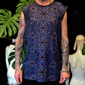 Può includere: Canotta nera con un motivo geometrico nei toni del blu, viola e rosa. Il design presenta forme ripetute a forma di stella. La maglietta ha uno scollo tondo. La persona che indossa la maglietta ha tatuaggi.