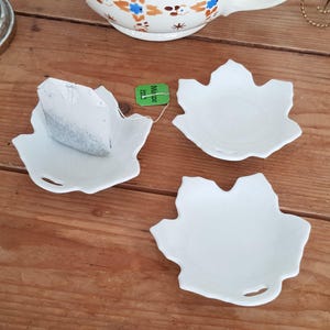 Könnte beinhalten: Drei weiße, keramikförmige, blattförmige Schalen, eine mit einem Teebeutel darin. Der Teebeutel ist grau und hat den Aufdruck "Milze".