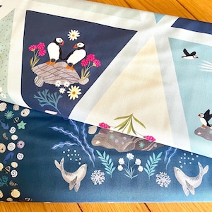 May include: A blue and white fabric featuring a design of sea creatures, including puffins, seals, and a lighthouse. The fabric is folded in half, displaying both sides of the pattern.