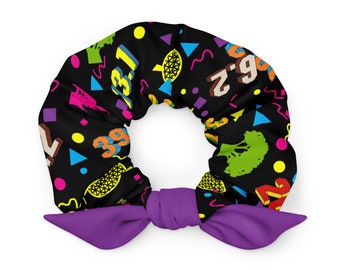 May include: A purple scrunchie with a black background and a colorful pattern of numbers, geometric shapes, and broccoli.