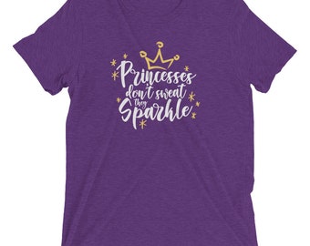 May include: Purple short-sleeved t-shirt with a white graphic that says "Princesses don't sweat they sparkle" with a gold crown above the text.