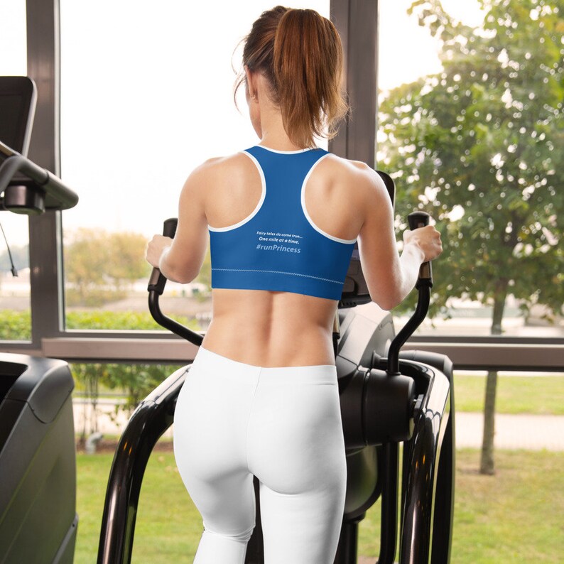 May include: A woman wearing a blue sports bra with white trim and the text "Every mile deserves a run. One mile at a time. #runPrincess". She is working out on an elliptical machine in a gym.