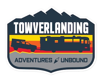May include: A blue and gray sticker with a silhouette of a truck towing a camper. The sticker says "Towverlanding Adventures Unbound" with a compass icon.