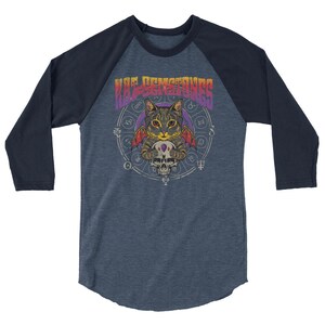 May include: A blue and navy blue baseball tee shirt with a graphic of a cat with wings holding a skull. The cat is surrounded by a circle of astrological symbols. The text "Bad Circumstances" is written in a rainbow gradient above the cat.