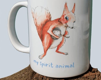 Puede incluir: Taza de cerámica blanca con una ardilla roja sosteniendo una nuez. La ardilla tiene ojos azules y una cola blanca. La taza tiene el texto "my spirit animal" en letras azules.