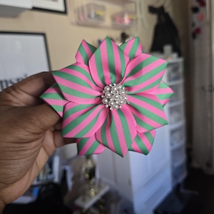 May include: A pink and green striped fabric flower with a pearl and rhinestone embellishment in the center.