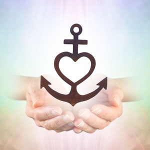 Könnte beinhalten: Ein schwarzer Anker mit einem Herzen in der Mitte, gehalten in den gefalteten Händen einer Person. Der Hintergrund ist ein weicher, verschwommener Regenbogen aus Farben.