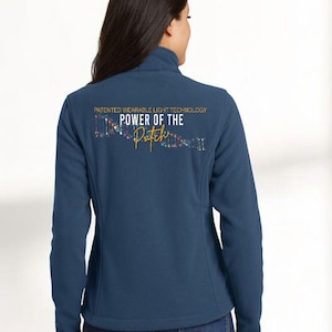 May include: A navy blue fleece jacket with a high collar. The back of the jacket features the text "POWER OF THE PATH" in gold and a colorful graphic. The jacket is worn by a person.