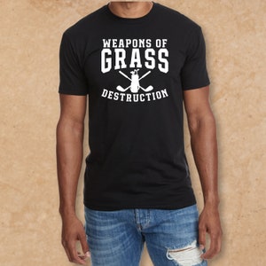 May include: A black t-shirt with white text that reads "Weapons of Grass Destruction" and a graphic of a golf bag with crossed golf clubs.