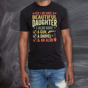 May include: A black t-shirt with a vintage-style graphic that reads "Yes I do have a beautiful daughter. I also have a gun, a shovel, & an alibi."