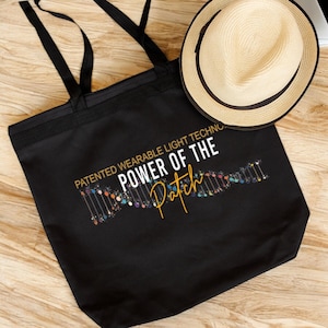 May include: Black tote bag with a white and gold graphic that says "Patented Wearable Light Technology Power of the Patch". The graphic also includes a colorful design of a DNA strand.