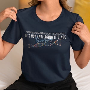 May include: A navy blue t-shirt with the text "PATENTED WEARABLE LIGHT TECHNOLOGY IT'S NOT ANTI-AGING IT'S AGE REVERSING" and a colorful graphic of a DNA strand.