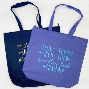 May include: Two tote bags, one blue and one purple, with the text "Love Them Spoil Them Give Them Back #Grammy" printed on the purple bag.