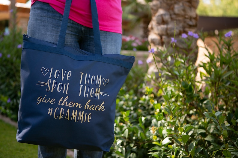 May include: A navy blue tote bag with gold lettering that reads "Love Them, Spoil Them, Give Them Back #Grammy".