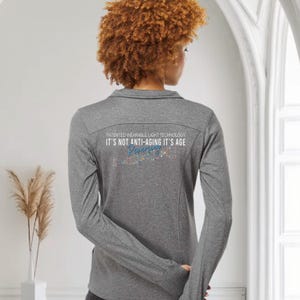 May include: A gray long-sleeved shirt with a collar and the text "PATENTED WEARABLE LIGHT TECHNOLOGY IT'S NOT ANTI-AGING IT'S AGE" printed on the back. The shirt has a colorful design below the text.