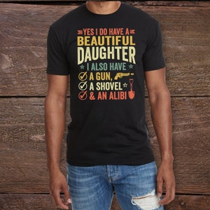 May include: A black t-shirt with a vintage-style graphic that reads "Yes I do have a beautiful daughter. I also have a gun, a shovel, & an alibi."
