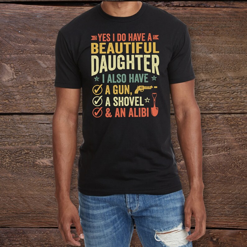 May include: A black t-shirt with a vintage-style graphic that reads "Yes I do have a beautiful daughter. I also have a gun, a shovel, & an alibi."