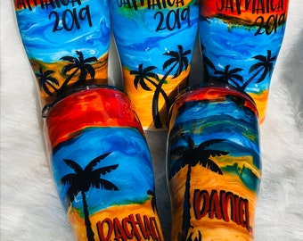 May include: Five colorful stainless steel tumblers with a beach scene and the words "Jamaica 2019" on the top. The tumblers have different names on the bottom, including "Daniel", "Pacha", and "Jamaica 2019".