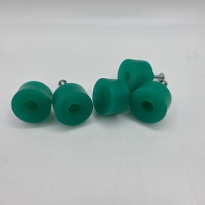 May include: A collection of six teal-colored, cylindrical bushings with a central hole, each affixed with a silver-colored bolt. The bushings are arranged on a white surface, showcasing their uniform shape and vibrant color.