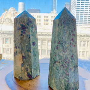 May include: Two green and blue gemstone towers with red flecks. The towers are on a wooden surface.