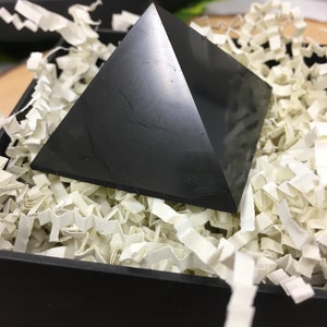 May include: Black obsidian pyramid crystal resting in white shredded paper inside a black box.