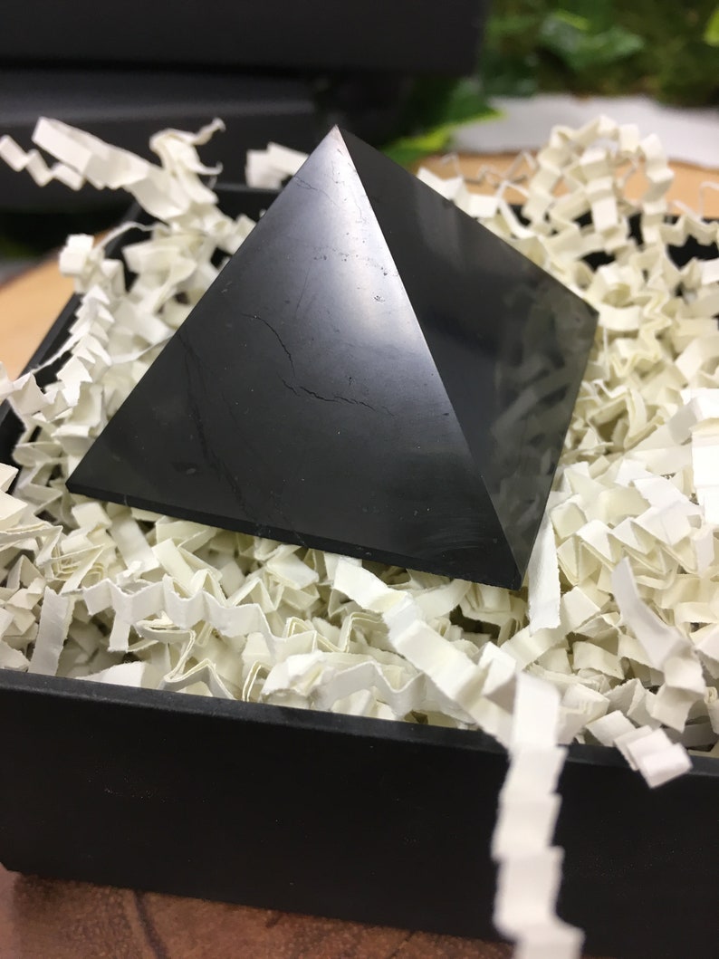 May include: Black obsidian pyramid crystal resting in white shredded paper inside a black box.