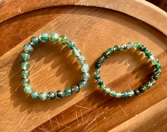 May include: Two green agate stone bracelets with a mottled pattern. The bracelets are made of round beads and are stacked on top of each other.