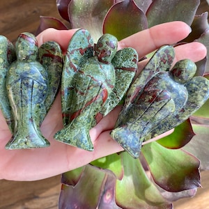 May include: Three green, red, and brown stone angel figurines. The angels are carved from a type of stone with a mottled pattern.
