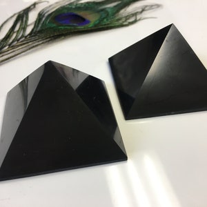 May include: Two black obsidian pyramids on a white surface. The pyramids are smooth and polished.