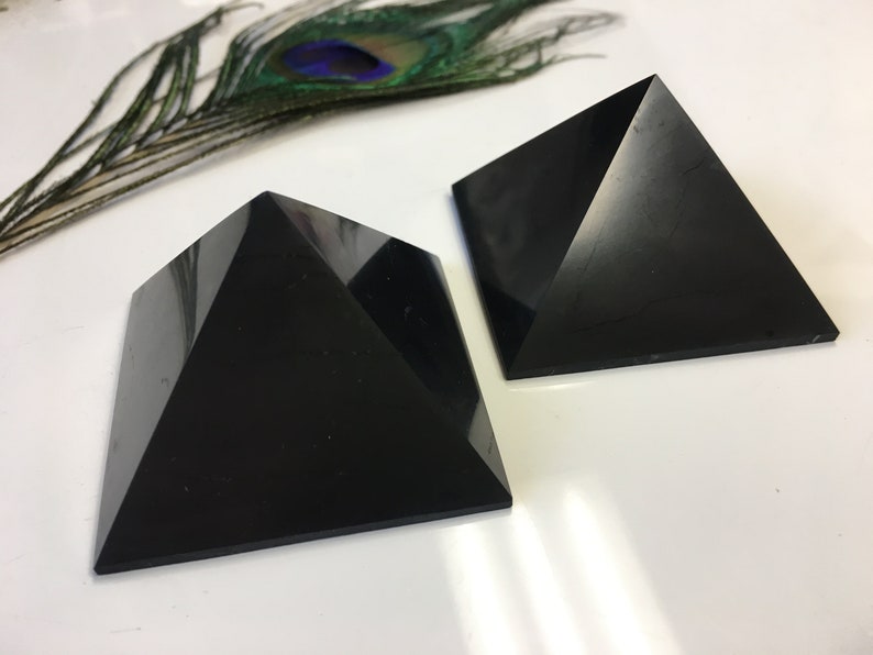 May include: Two black obsidian pyramids on a white surface. The pyramids are smooth and polished.