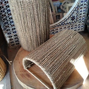 May include: Two woven baskets made of natural rope, one is cylindrical and the other is a half-cylinder shape. The baskets are sitting on a wooden surface.