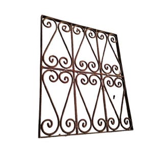 Puede incluir: Una reja de ventana de metal decorativa con un patrón geométrico de espirales entrelazadas. La reja está hecha de hierro y tiene un acabado rústico y envejecido.