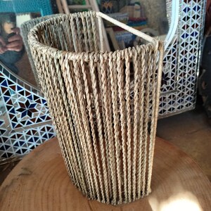 May include: A woven lampshade made of natural fibers, with a curved shape and a light brown color.