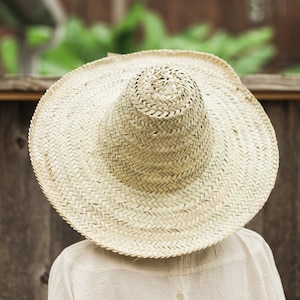 May include: A large, wide-brimmed straw hat with a woven texture. The hat is light brown and has a slightly rounded crown.