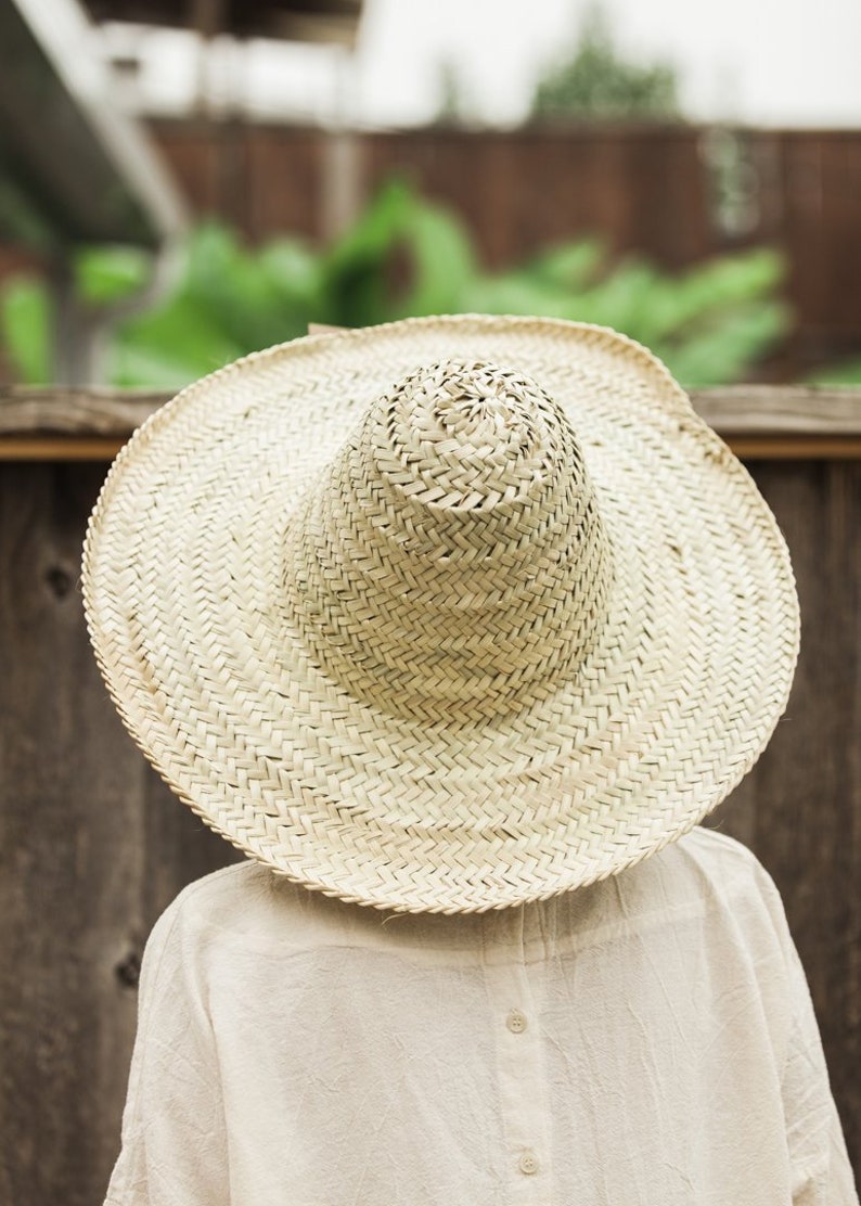 May include: A large, wide-brimmed straw hat with a woven texture. The hat is light brown and has a slightly rounded crown.
