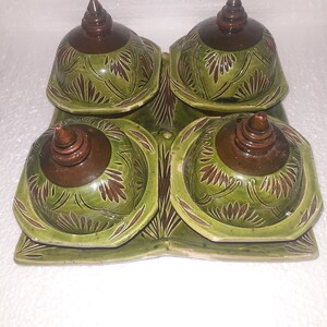 May include: A set of four green ceramic bowls with brown lids. The bowls have a floral design and are arranged on a matching green tray.