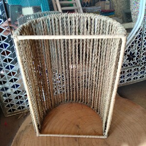 May include: A beige woven cylindrical lampshade with a rectangular opening at the top and bottom. The lampshade is made of natural fibers and has a rustic look.