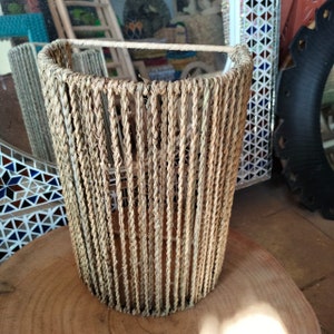 May include: A woven lampshade made of natural fibers, with a cylindrical shape and a light brown color.