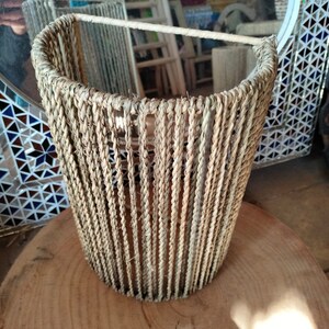 May include: A half-round, woven basket made of natural fibers. The basket is made of a light brown material and has a smooth, even texture. The basket is empty and is sitting on a wooden surface.
