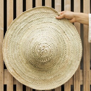 May include: A large, round, woven straw hat with a wide brim. The hat is light brown and has a natural, rustic look.