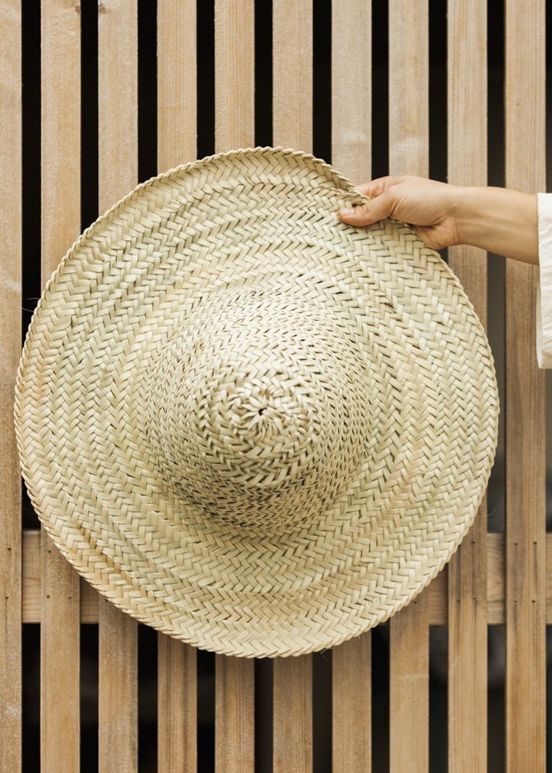 May include: A large, round, woven straw hat with a wide brim. The hat is light brown and has a natural, rustic look.