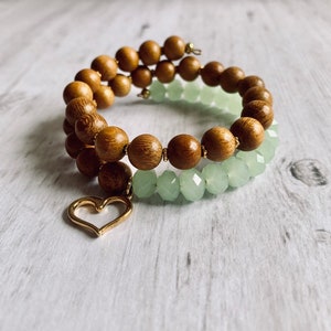 May include: A double-strand bracelet with wooden beads and light green glass beads. A gold heart charm hangs from the bracelet.