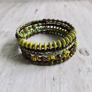 May include: A multi-strand bracelet with green, brown, and gold beads. The bracelet is made of several layers of beads, creating a layered effect.